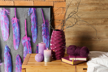 Burning candles with books and knitting yarn on wooden table in bedroom