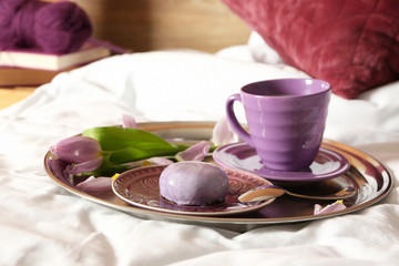 Tray with cup of coffee, cake and flower on bed