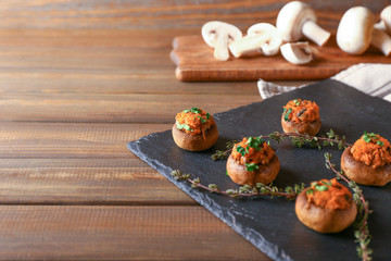 Slate plate with tasty stuffed mushrooms on wooden table