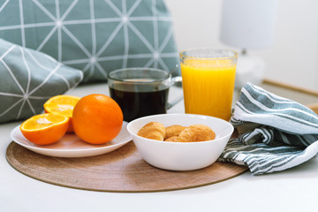 Morning breakfast in bed, hotel room. Croissants, black coffee, oranges and juice on the wooden tray.