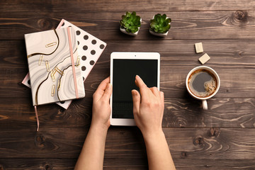 Female hands with tablet computer, cup of coffee and notebooks on wooden background