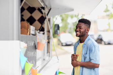 street sale and people concept - happy smiling male customer looking at billboard at food truck