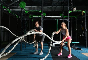Young sporty couple doing battle rope exercise in gym