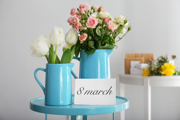 Jugs with beautiful flowers for International Women's Day on table