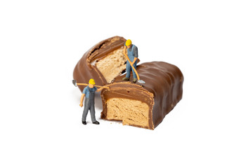 Miniature Workers Working On Top Of Nougat Chocolates, Isolated On White Background