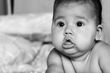 A beautiful toddler girl with dark eyes of Indian appearance is lying on the bed