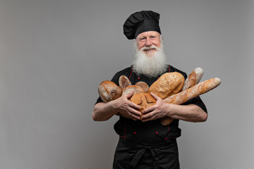 Cheerful baker wearing a uniform holding with fresh bread from on grey background
