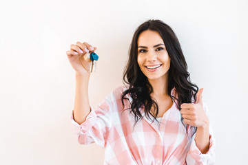 cheerful woman holding key while showing thumb up isolated on white