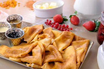 Russian traditional pancakes, blini. Served with jams, sour cream, milk and strawberry on the plate. Side view.