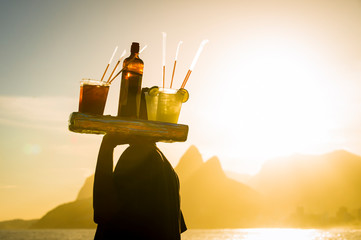 Scenic sunset view of Two Brothers Mountain with an unrecognizable silhouette of a beach vendor carrying caipirinha cocktails passing in silhouette at Arpoador in Rio de Janeiro, Brazil - 251994246