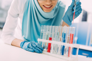 cropped view of smiling female muslim scientist adding blood in test tube in laboratory