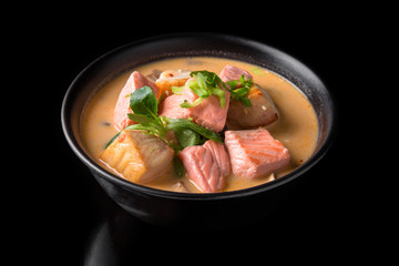 Spicy Thai soup Tom Yam with Coconut milk, Chili pepper and Seafood shrimp and salmon in a plate on a black background. Asian cuisine, restaurant menu.