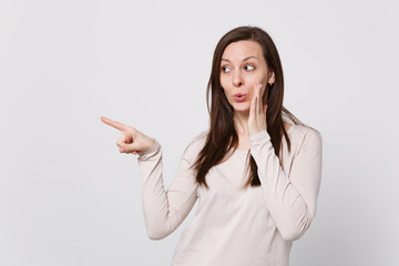 Pretty young woman in light clothes holding hand near face, looking pointing index finger aside isolated on white background in studio. People sincere emotions, lifestyle concept. Mock up copy space.