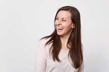 Obraz premium Portrait of laughing joyful attractive young woman in light clothes standing, looking aside isolated on white wall background in studio. People sincere emotions lifestyle concept. Mock up copy space.