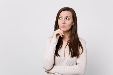 Portrait of pensive young woman in light clothes looking aside, put hand prop up on chin isolated on white wall background in studio. People sincere emotions, lifestyle concept. Mock up copy space.