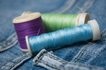 closeup of sewing thread spool bobbin on blue jeans background