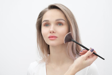 Make-up artist makes makeup beautiful blonde girl on a white background. Close-up hands with brush and face.