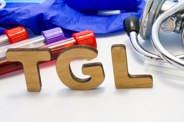 TGL abbreviature mean triglyceride simple blood test  with lab tubes with blood and stethoscope. Using acronym TGL in laboratory clinical diagnosis, measure the level of triglycerides in blood