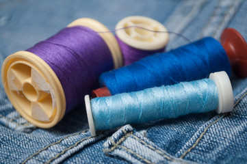 closeup of sewing thread spool bobbin on blue jeans background