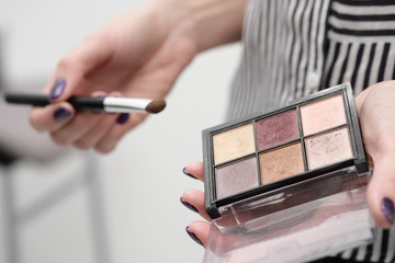 Makeup artist's tools in his hands, mascara, shadows and brush on a white background.