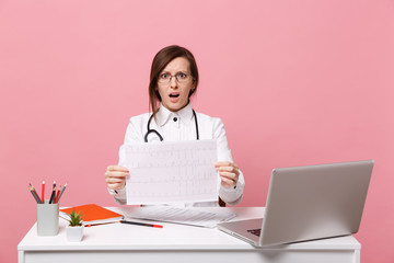 Female doctor sits at desk works on computer with medical document heart ekg in hospital isolated...