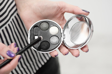 Makeup artist's tools in his hands, mascara, shadows and brush on a white background.