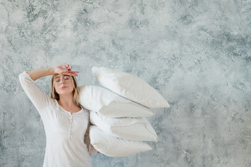 Morning duties. Arranging bedding. Tired young woman holding pile of pillows. Copy space on grey...