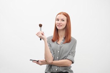 Portrait of a red-haired girl, make-up of actor, professional on white background. Paint brushes and palette in hand.