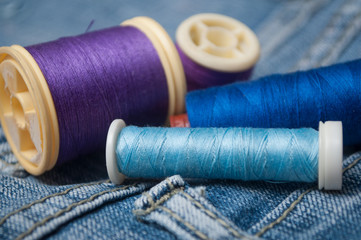 closeup of sewing thread spool bobbin on blue jeans background