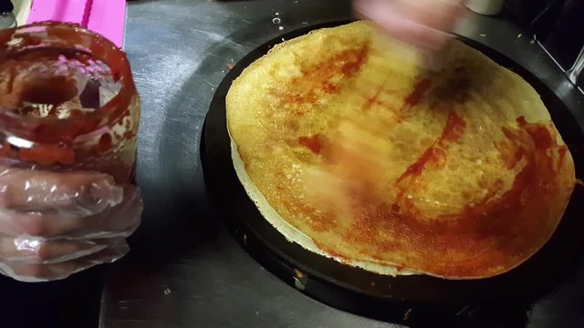 Male cook putting some tomato sauce on crepe on a black cooker for preparation. 