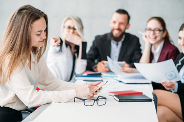 Business meeting. Paperwork. Team members laughing at daydreaming colleague checking smartphone.