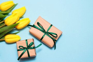 A bouquet of yellow tulips and two craft gifts on a blue paper background. pring background,...