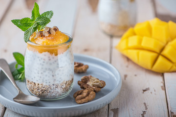 Homemade pudding of Chia seeds and almond milk with cereals and puree of mango and kiwi with walnuts and mint in glass jars. Vegan healthy morning breakfast or superfood dessert