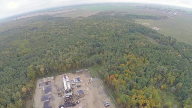 Multicolored autumn forest. Industrial oil pump jack working and pumping crude oil for fossil fuel energy with drilling rig in oil field. Aerial photography slide.