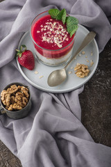 Top view of Homemade pudding of Chia seeds and almond milk with cereals and puree strawberry with walnuts and mint in glass jar. Vegan healthy morning breakfast or superfood dessert