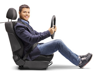 |Young man in a car seat with a fastened seat belt holding a streering wheel