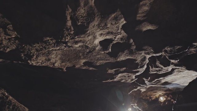 View of cave rocky ceiling and tunnel illuminated with lamplights and caver man standing