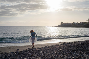 Girl viewed from rear dancing at the beach with ocean in background - vacation and happiness concept for people love freedom and nature