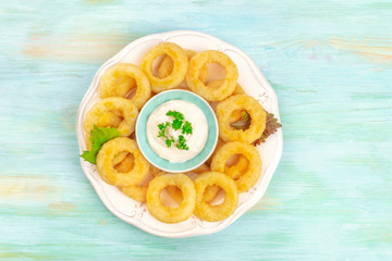 An overhead photo of a plate of calamari rings with a dip and a place for text, shot from the top on a blue background