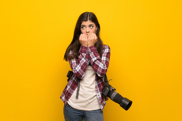 Fototapeta na wymiar Photographer teenager girl over yellow wall nervous and scared putting hands to mouth