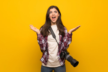 Photographer teenager girl over yellow wall with shocked facial expression