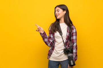 Photographer teenager girl over yellow wall pointing to the side to present a product