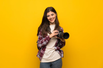 Photographer teenager girl over yellow wall smiling