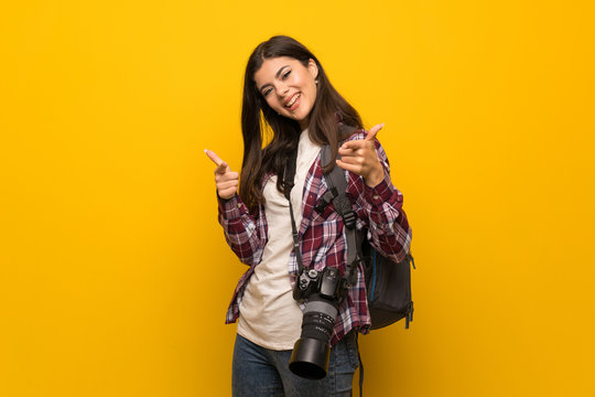 Photographer teenager girl over yellow wall pointing to the front and smiling