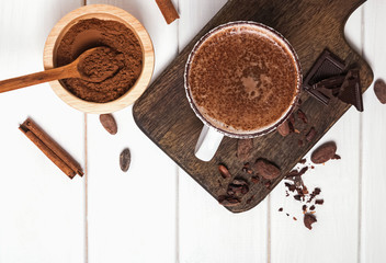 Hot chocolate in the cup, cocoa beans and powder on the white wooden table