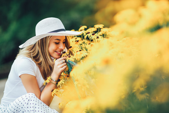 Beautiful young woman smelling yellow flower in the park.