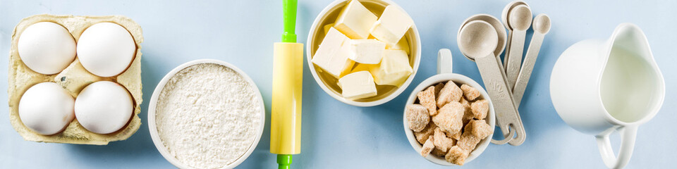 Baking ingredients and tools on trendy bright blue background - flour, eggs, sugar, milk, butter, layout, flatlay top view copy space banner