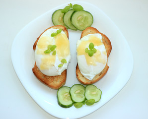 Poached eggs on toasted baguette slices.with a cucumber on a white plate