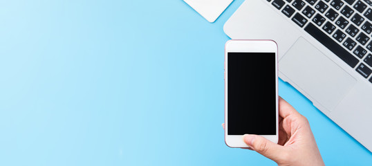 A woman is holding a smartphone isolated with a minimal blue desk, concept of online shopping payment, internet work at home, e-commerce, copy space, flat lay, top view, mock up