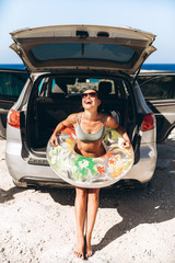 Pretty pan asian brunette with float near car trunk at the seaside beach.